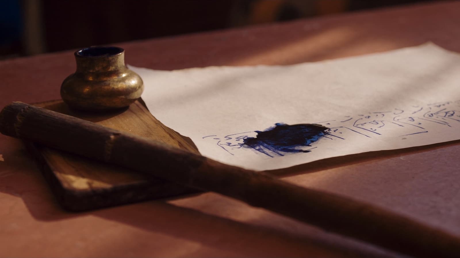 A reed qalam and inkwell on a writing board.